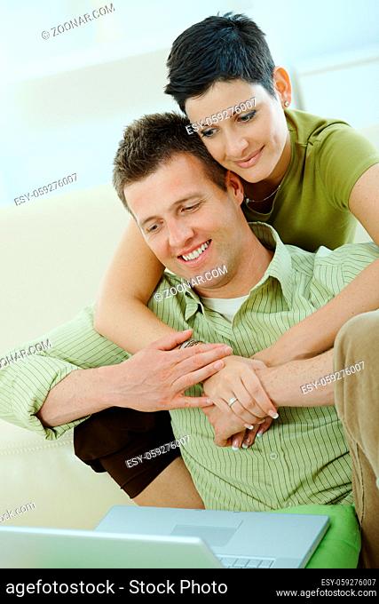 Love couple using laptop computer at home, woman hugging man, smiling