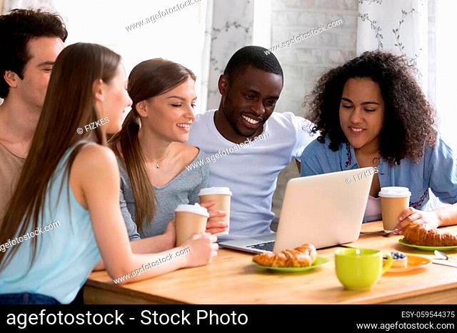 Smiling diverse people, group of happy young women and men sitting together at table in cafe, looking at laptop screen, watching comedy movie or funny videos in...