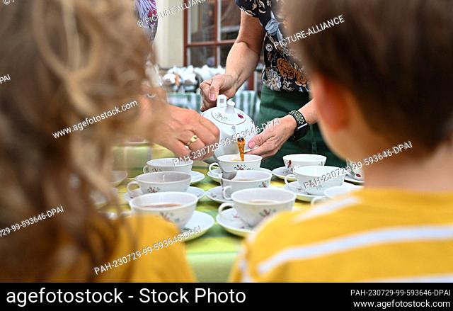 29 July 2023, Lower Saxony, Leer: Two employees of the tea museum pour tea East Frisian style under the eyes of two young guests
