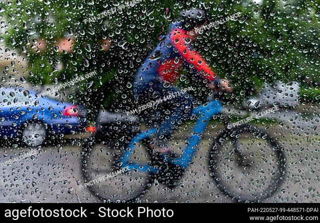 27 May 2022, Saxony, Leipzig: A cyclist is seen behind a window with raindrops in Leipzig. After the dryness of the past weeks, Friday starts with rain
