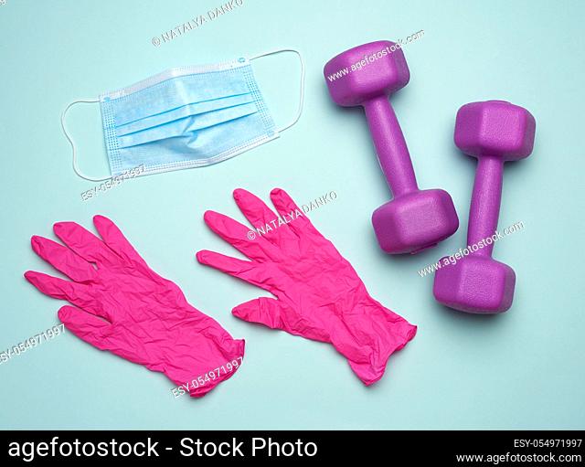 plastic dumbbells, a medical mask and pink latex gloves. The concept of doing sports in protective equipment on a blue background, flat lay