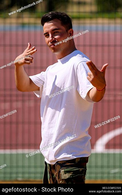 Man gesturing finger gun standing in front of sports court on sunny day