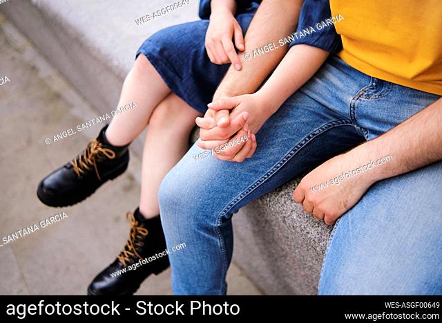 Young couple holding hands while sitting together on wall