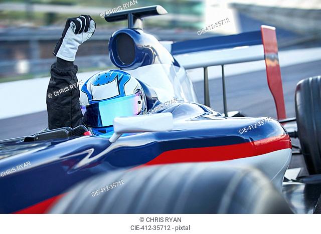 Portrait formula one race car driver wearing helmet and cheering with fist on sports track