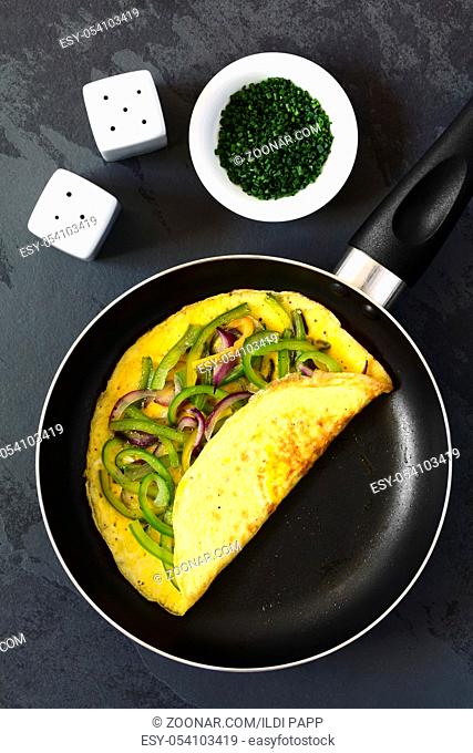Omelette with green bell pepper and red onion in frying pan, photographed overhead on slate with natural light