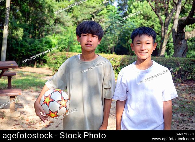 Two 13 year old boys in a park with a football in summer