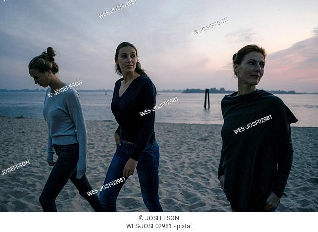 Germany, Hamburg, mother with two teenage girls walking on the beach at Elbe shore in the evening