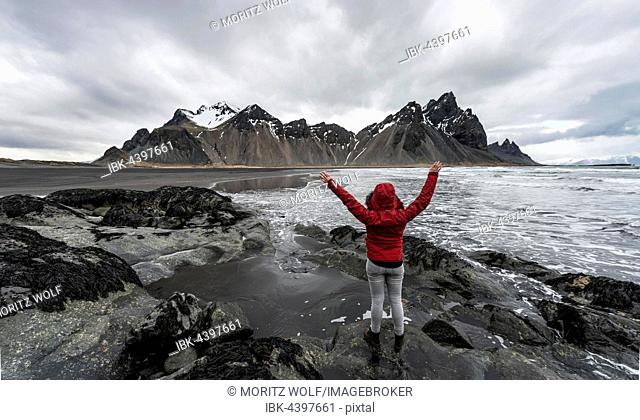 Hiker with arms outstretched, mountains Klifatindur, Eystrahorn and Kambhorn, Stokksnes headland, Klifatindur mountain range, Eastern Region, Iceland