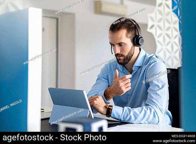 Young professional with headphones talking on video call over digital tablet at office