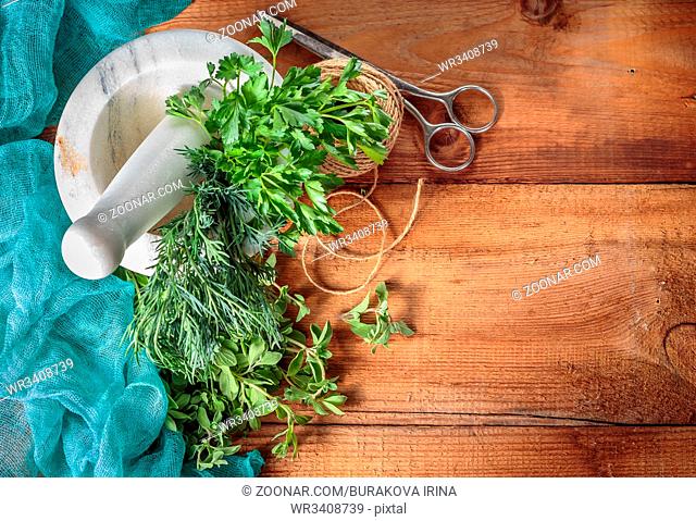 Spicy grass marjoram, dill, parsley, scissors and marble mortar on a wooden table. Top view