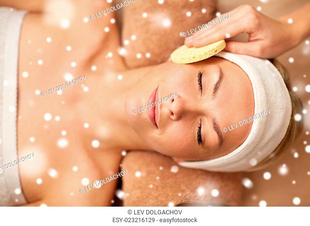people, beauty, spa, healthy lifestyle and relaxation concept - close up of beautiful young woman lying with closed eyes and having face massage with sponge in...