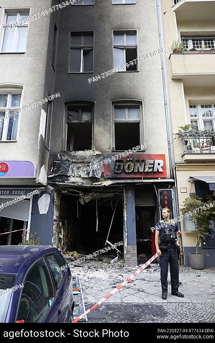 27 August 2023, Berlin: A policeman stands in front of a burnt-out kebab restaurant in Uhlandstraße. According to the police spokesman