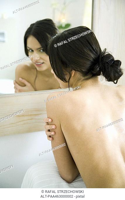 Young woman looking into bathroom mirror