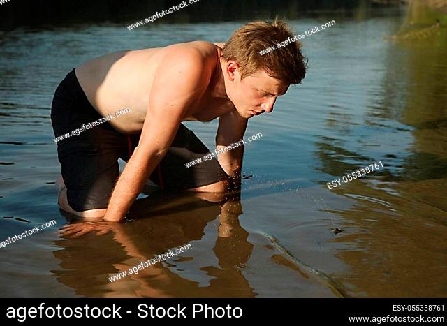 Young man observing clam squirting water in the shallow waters of a river