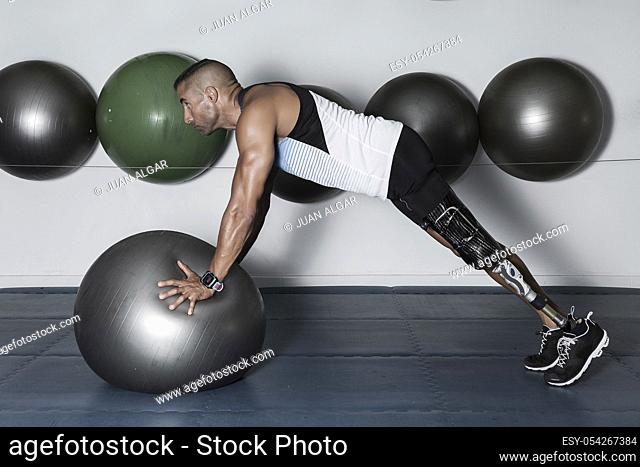 Side view of concentrated sportsman with leg limb training with medicine ball in gym