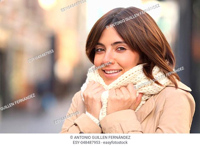 Happy woman being cold grabbing scarg and looking at camera in winter in the street