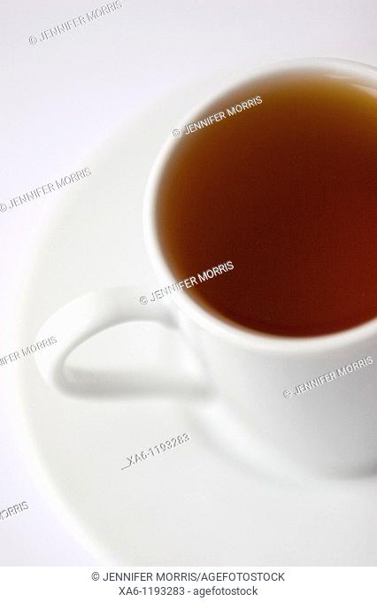 A white cup of black rooibos tea rests on a saucer against a white background