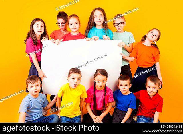 The group of kids holding a big white copy space poster at the yellow background