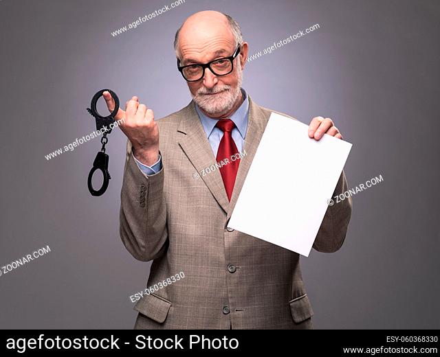 Senior business man with handcuffs and blank contract paper hints at danger of financial crimes