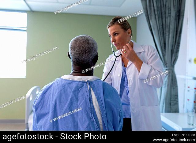 Caucasian female doctor examining with stethoscope african american male patient in hospital room