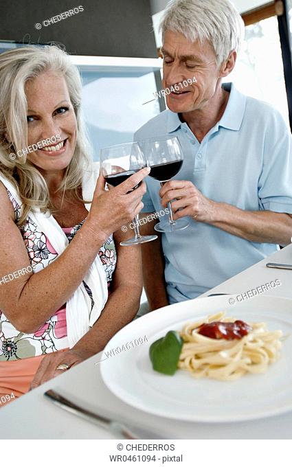 Close-up of a senior couple toasting with wine glasses and smiling at the kitchen counter