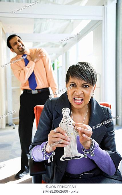 Angry African businesswoman holding voodoo doll of co-worker