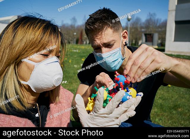 Asian woman with a protective mask with virus models on her hands and a Caucasian guy points at them. The concept of Coronavirus