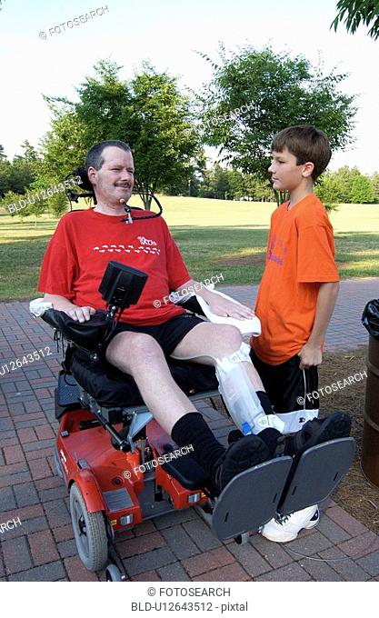 Man with significant disabilities, utilizing a powered wheelchair for mobility, spending time with his son in the park