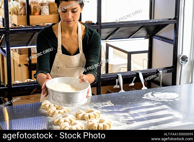 Medium shot of female Latin-American bakery owner sifting flour on her bread loaves
