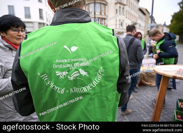 24 September 2022, Saxony-Anhalt, Halle (Saale): ""Regional=Climate Neutral"" is written on a fruit grower's vest. The region's growers handed out free fruit to...
