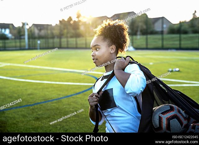 UK, Rear view of female soccer player carrying bag with balls in field
