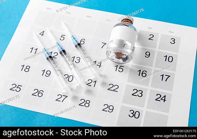disposable syringe and calendar on blue background