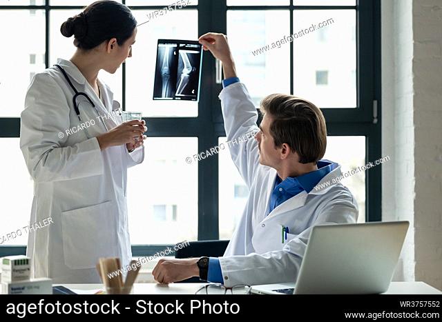 Young female physician using a tablet PC while asking for advice from her experienced male colleague in the office a modern hospital