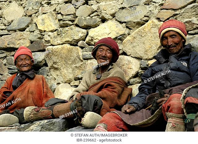 Three friendly man in traditional dress made of wool sit at a wall Phu Nar-Phu Annapurna Region Nepal