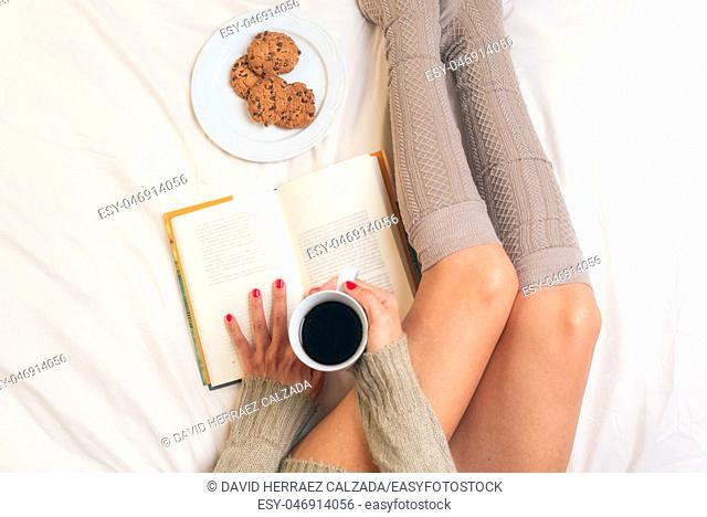 Woman eating breakfast in bed while reading a book
