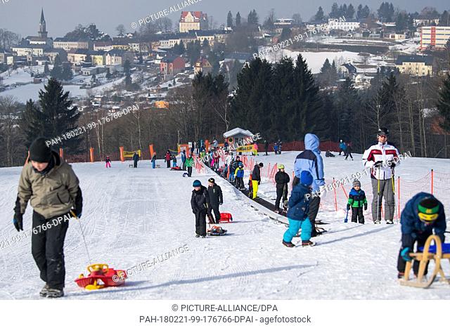 Winter sports aficionados riding a magic carpet lift up a hill in Schoeneck, Germany, 21 February 2018. Lugers pulling their sleds can be seen to the side