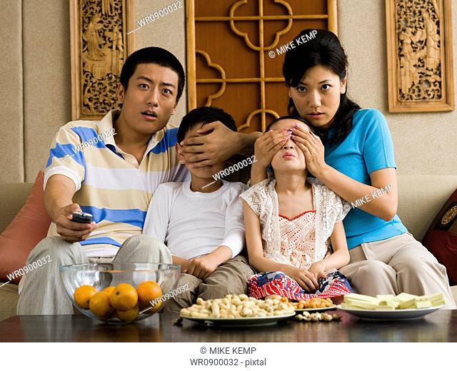 Family watching television with parents covering childrens eyes