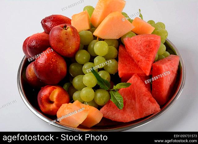 Fruit mix. Nectarine, grapes, watermelon, melon. Pieces of fruit on a plate lie on a silver tray on white background
