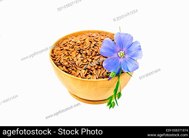 Brown flaxseeds in wooden bowl with blue flower isolated on white background