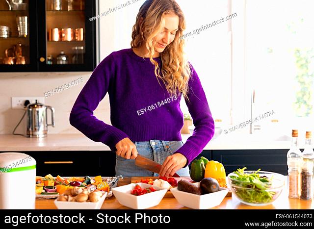 Smiling caucasian woman standing in kitchen chopping vegetables