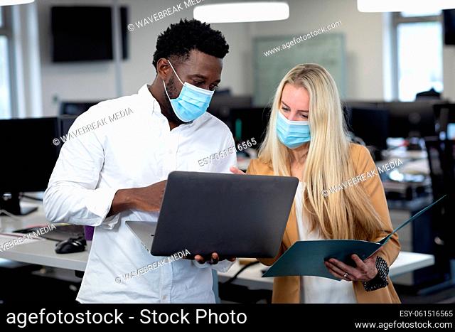 Businessman and businesswoman wearing face masks working together at modern office