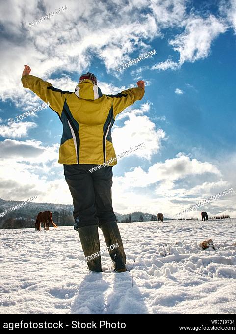 Woman in yelow black work clothes and rubber boots gesture in snow against Sun. Low angle view
