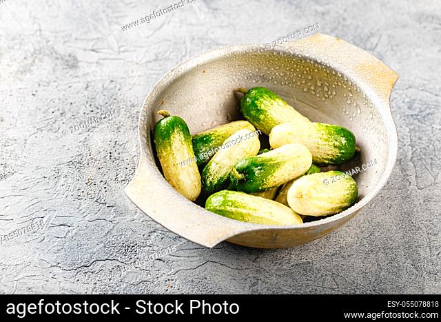 Baby cucumbers with unusual coloring in metal bowl on gray background, place for text