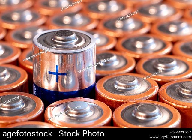 Multiple used AA alkaline batteries are seen arranged in a pile. Closeup side view from the plus side of the battery. Blue plus side of a battery