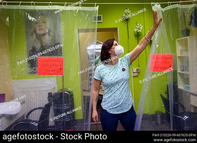 dpatop - 26 February 2021, Saxony-Anhalt, Magdeburg: Jacqueline Lucas, owner of ""Salon Stötzer"", pushes aside a protective curtain that stretches across the...