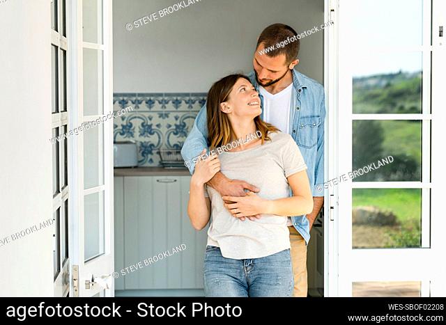 Attractive young couple standing in the door together at home and smiling at each other