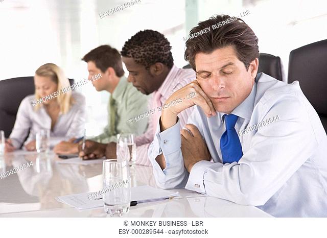 Four businesspeople in boardroom with one businessman sleeping