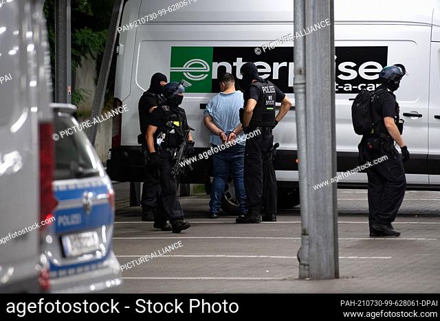 30 July 2021, Berlin: Police officers stand next to a perpetrator suspect on the grounds of a hardware store in Berlin-Wedding after his arrest