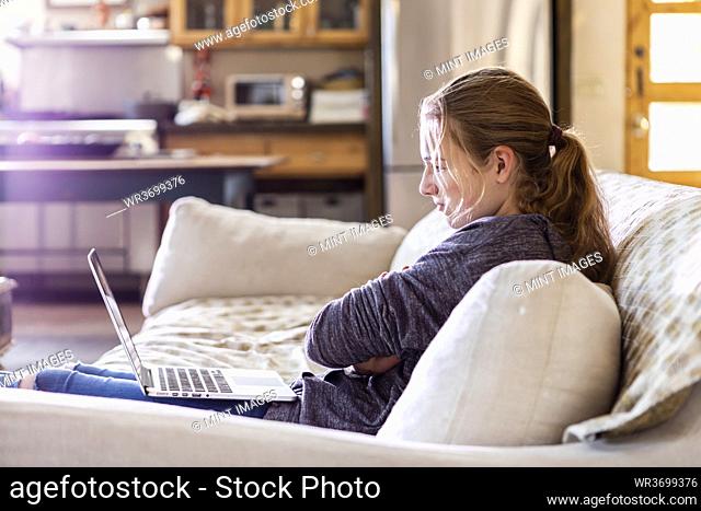 Teenage girl looking at laptop on sofa