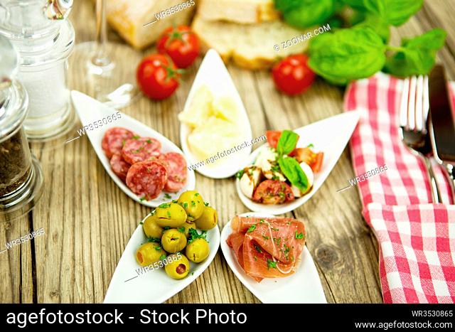 gemischte vorspeisenplatte mit parma parmesan tomaten oliven auf einem teller Holztisch